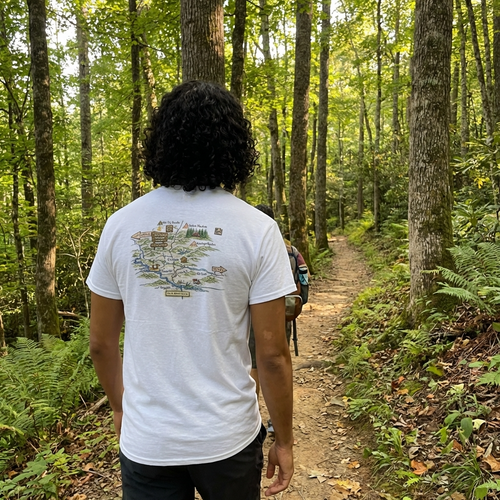 Person walking on a trail in a forest wearing a white t-shirt with a map design.